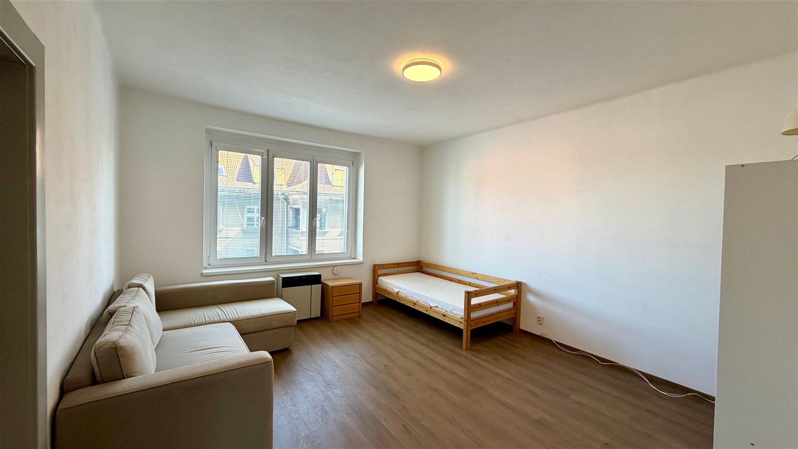 Světlý obývací pokoj s parketovou podlahou, velkými okny a moderním nábytkem, skýtající útulný prostor pro rodinné bydlení.