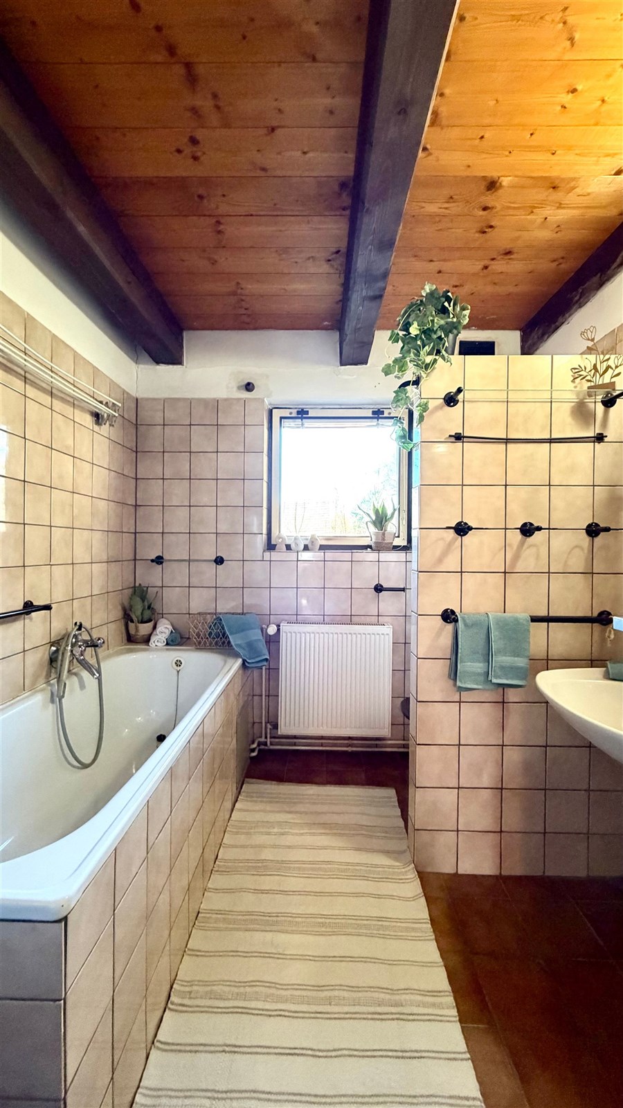 Koupelna s dřevěným stropem, světlá dlažba, velká okna. Rustikální styl s modernizovanými prvky, ideální pro relaxaci.