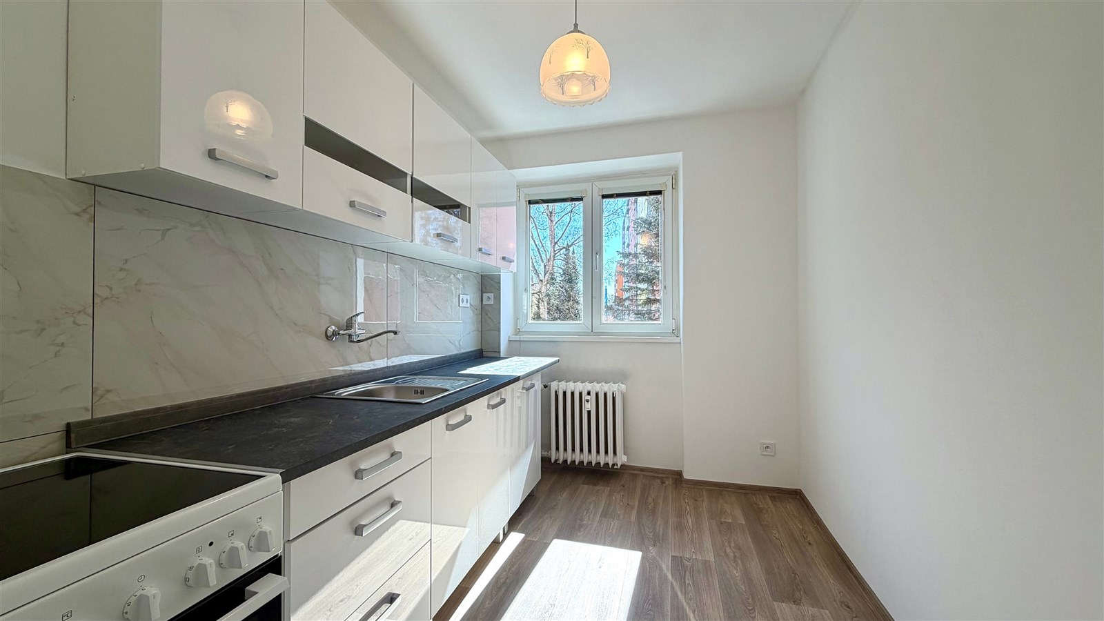 Moderní kuchyň s parketovou podlahou, světlá zařízení, velká okna, nová linka s bílými skříňkami a kameninovou deskou.