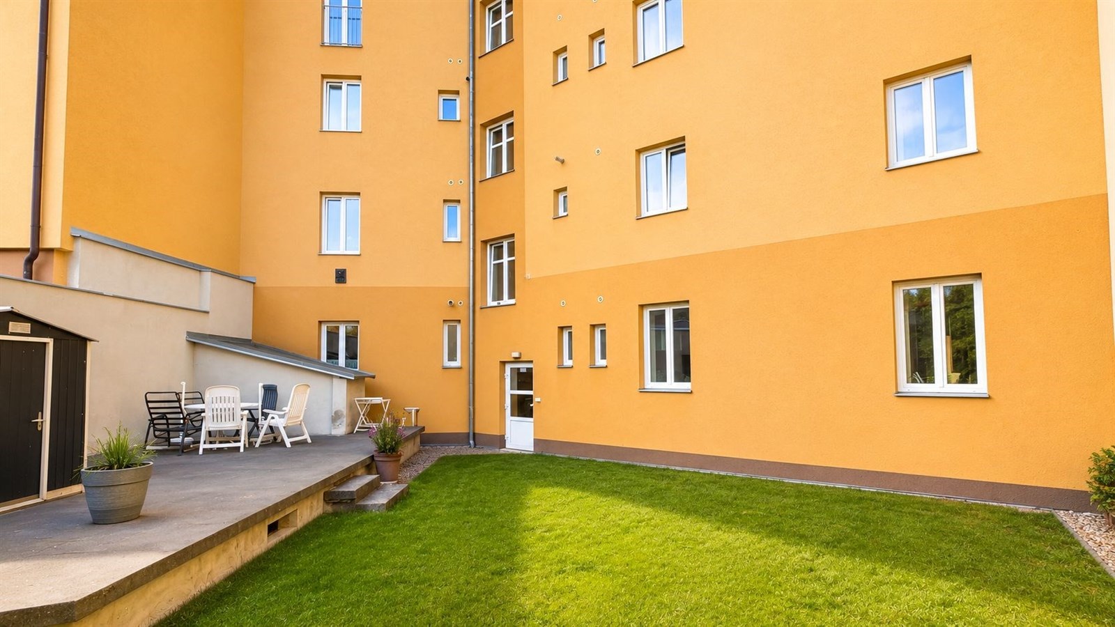 Venkovní dvůr s dobře udržovaným trávníkem, moderní fasáda budovy, velká okna pro přirozené osvětlení, ideální pro relaxaci venku.