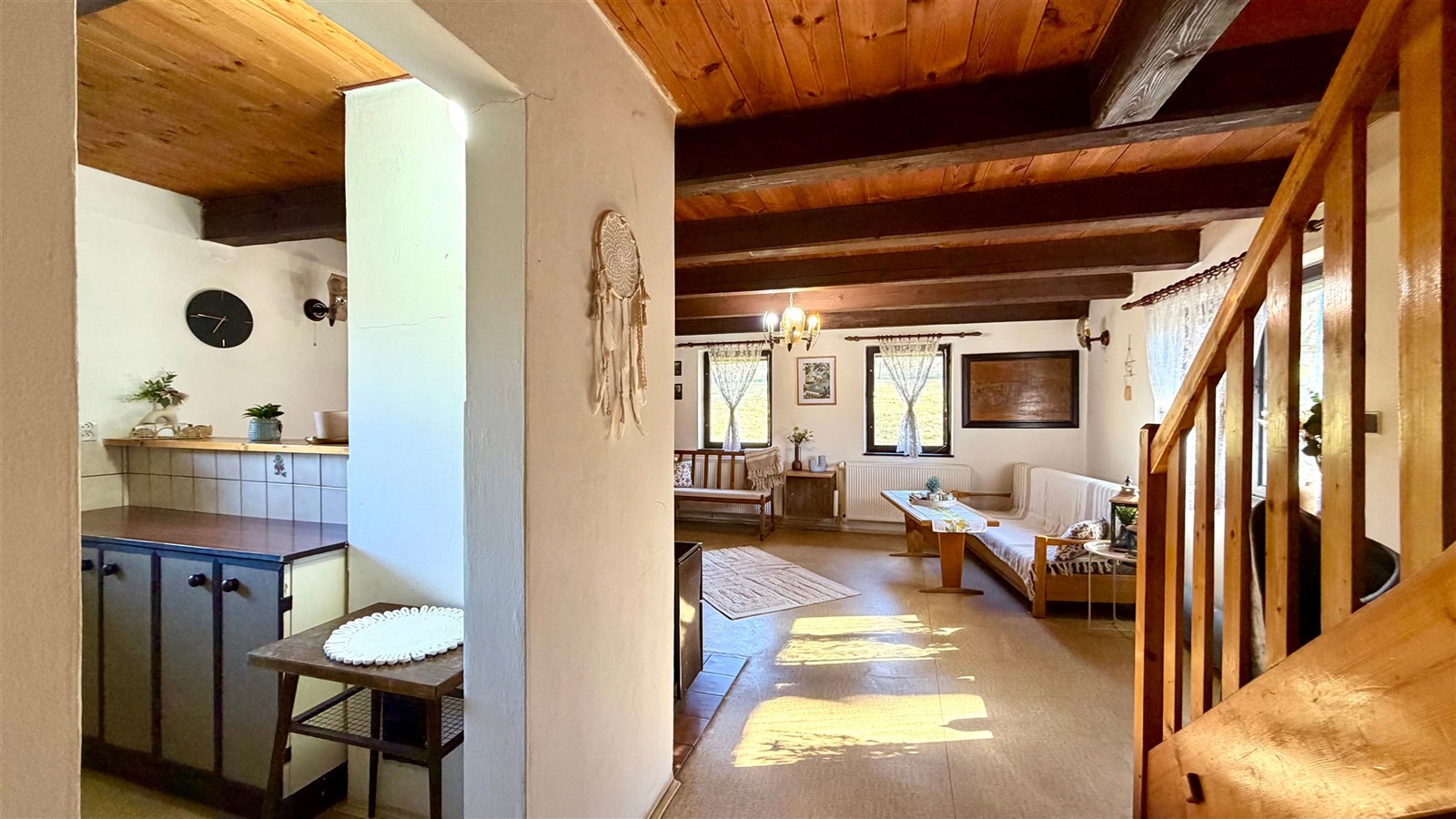 Světlý obývací pokoj s dřevěným stropem a parketovou podlahou, nabízí velká okna a rustikální styl.