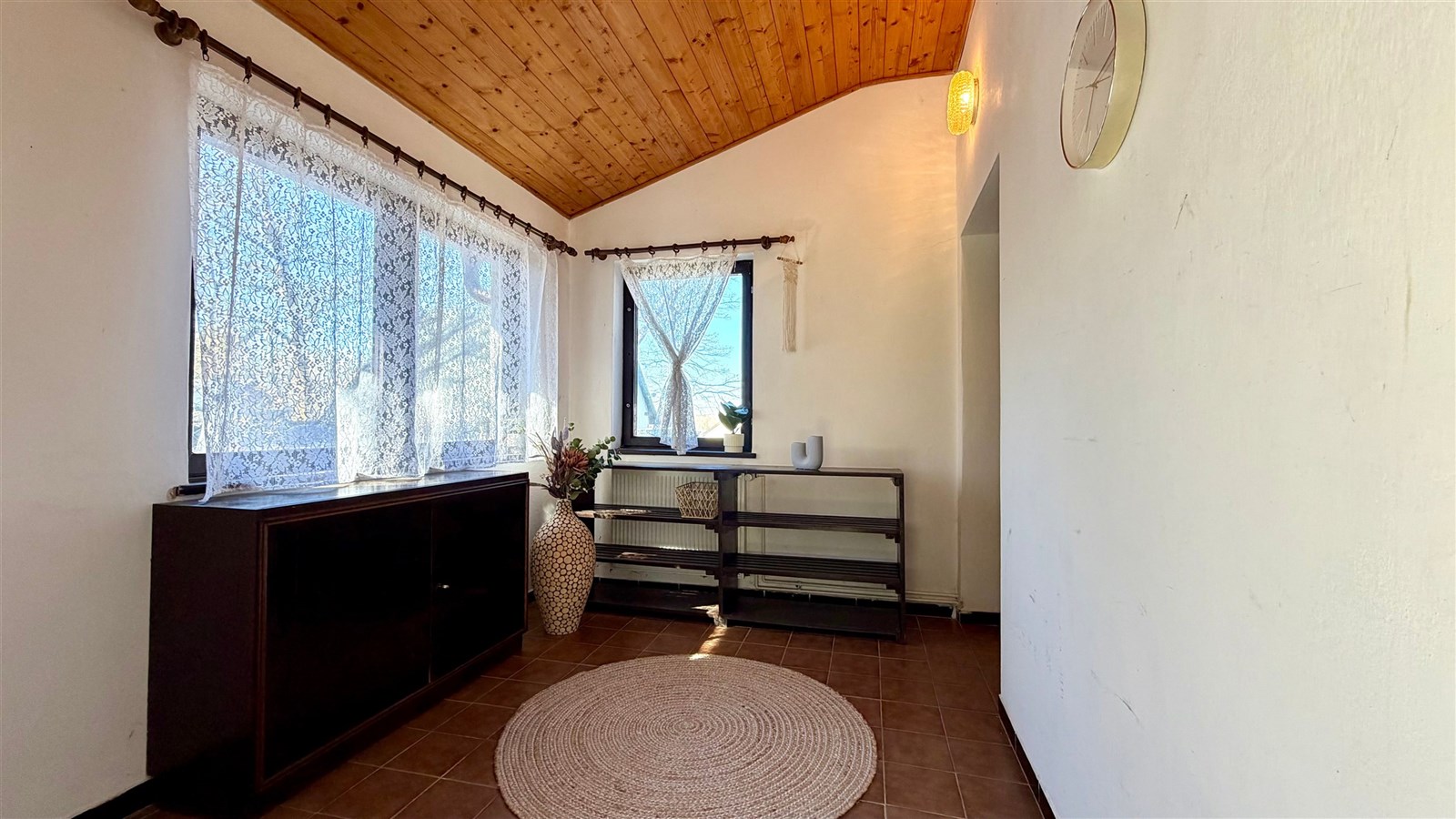 Světla veranda s dřevěným stropem, dlažbou a velkými okny. Jednoduchý moderní styl, ideální jako odpočinkový prostor.