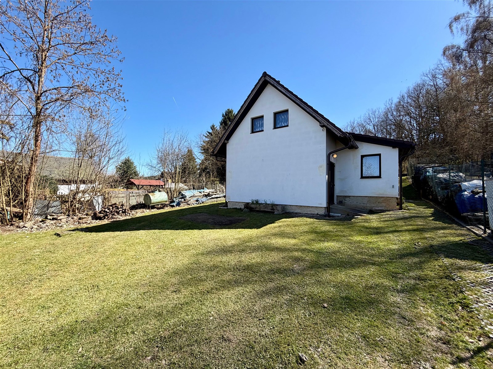 Exteriér domu s omítnutou fasádou a šikmou střechou, obklopený prostornou zahradou, ideální pro rodinné bydlení na klidném místě.