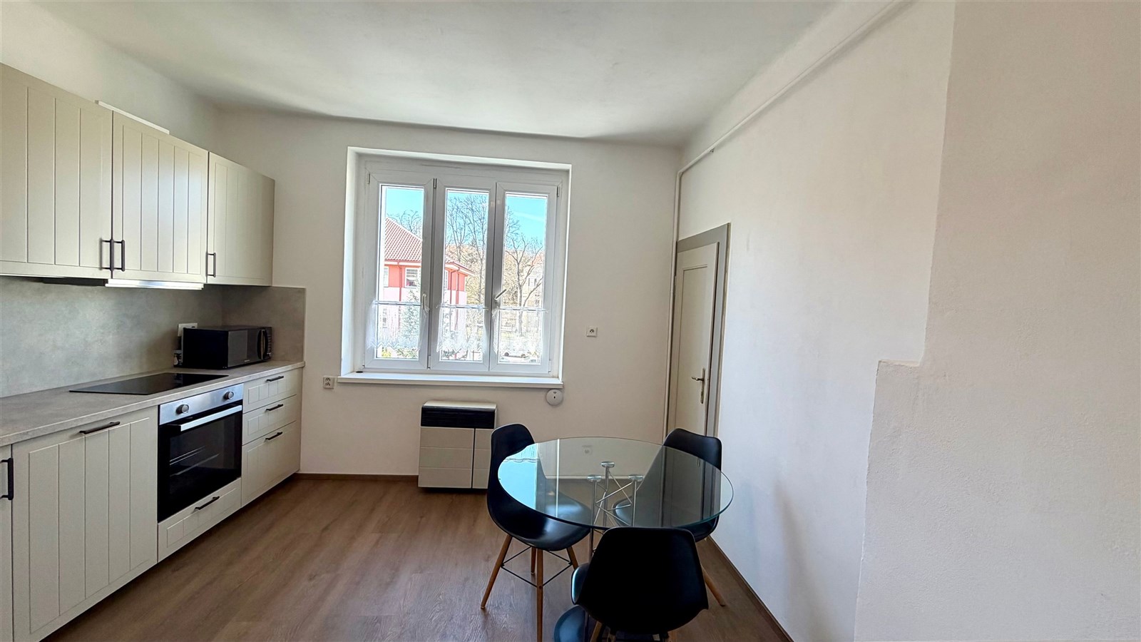 Moderní kuchyň s vestavěnými spotřebiči, parketová podlaha a velká okna poskytující dostatek světla