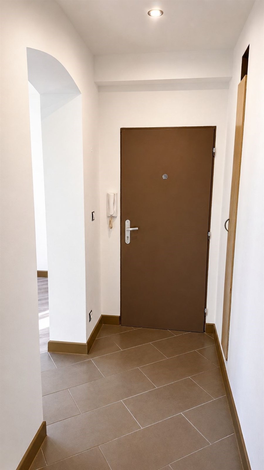 Vstupní chodba s dlažbou a moderními svítidly, vybavena bezpečnostními dveřmi, světlý interiér nabízí útulný pocit a okamžitý přístup do ostatních místností