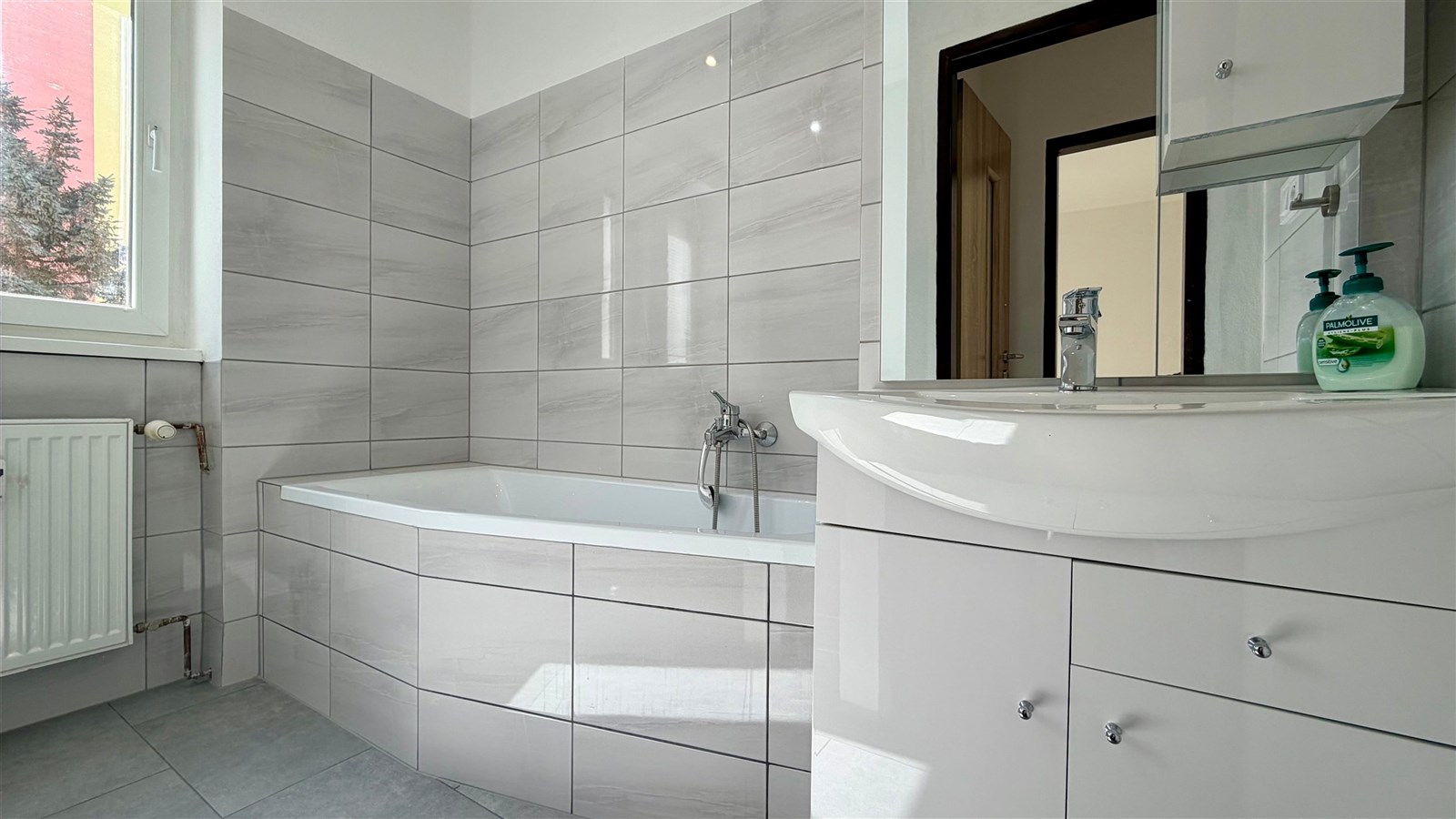 Moderní koupelna s velkou vanou, dlažbou a světlými obklady. Světlá a rekonstruovaná místnost zajišťuje pohodlné bydlení.