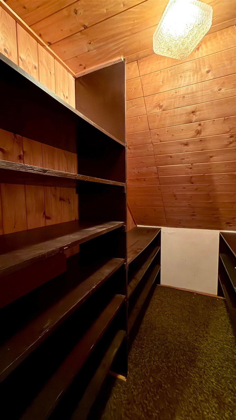 Podkrovní úložný prostor s dřevěnými obklady, vestavěné police, teplé osvětlení, ideální pro organizaci a skladování