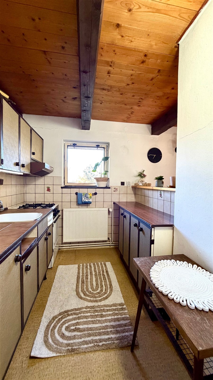 Kuchyně s dřevěným stropem, dlažbou a vestavěnými skříněmi, nabízí rustikální kouzlo a útulnou atmosféru.