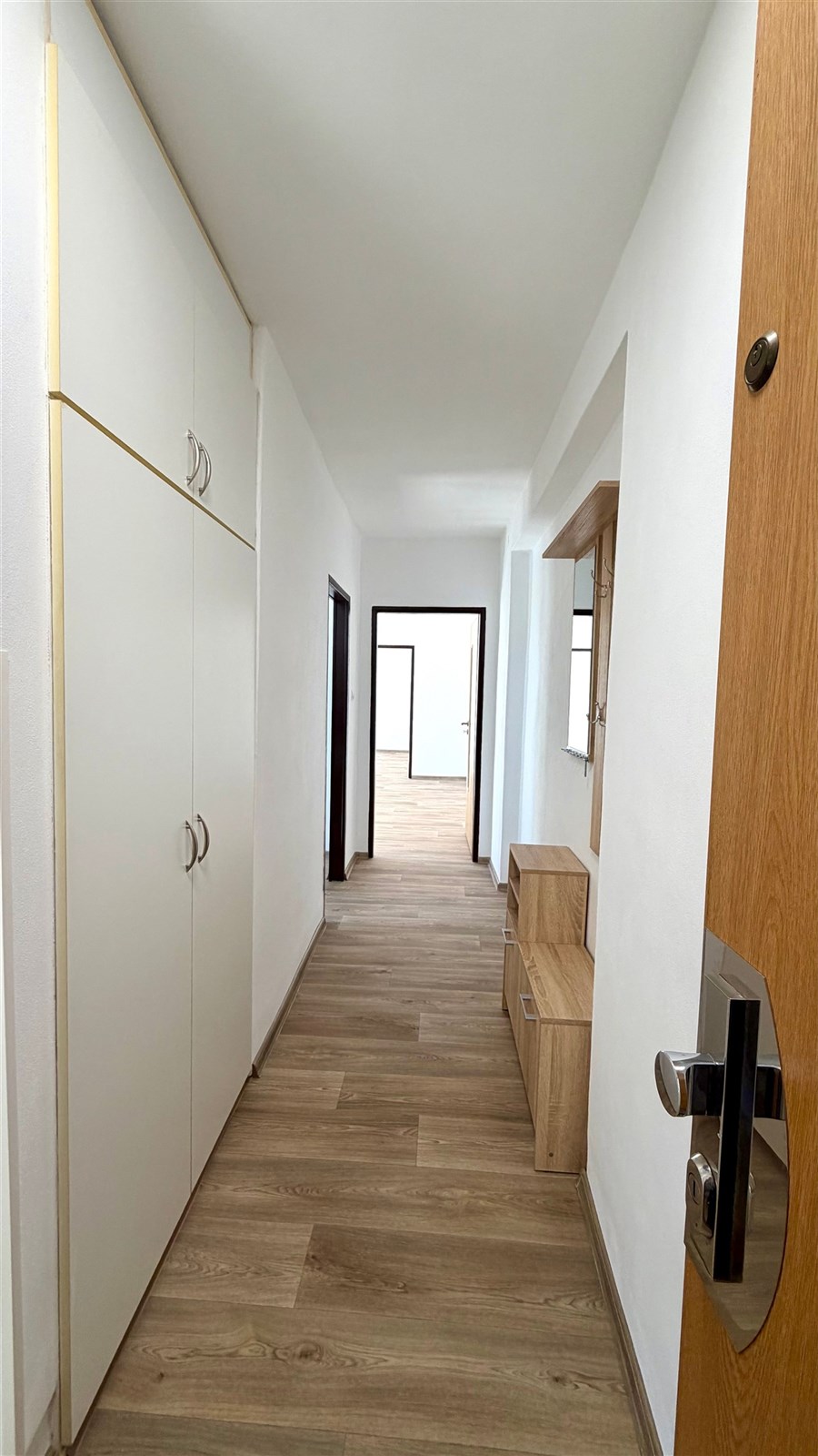 Světlá chodba s laminátovou podlahou, vestavěnými skříněmi a moderním dřevěným nábytkem, ideální pro uložení a organizaci věcí.