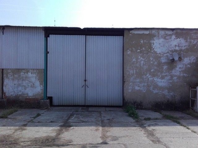 Průmyslové skladové prostory s plechovými vraty, betonovou podlahou a potřebou renovace, ideální pro skladovací účely nebo dílnu.