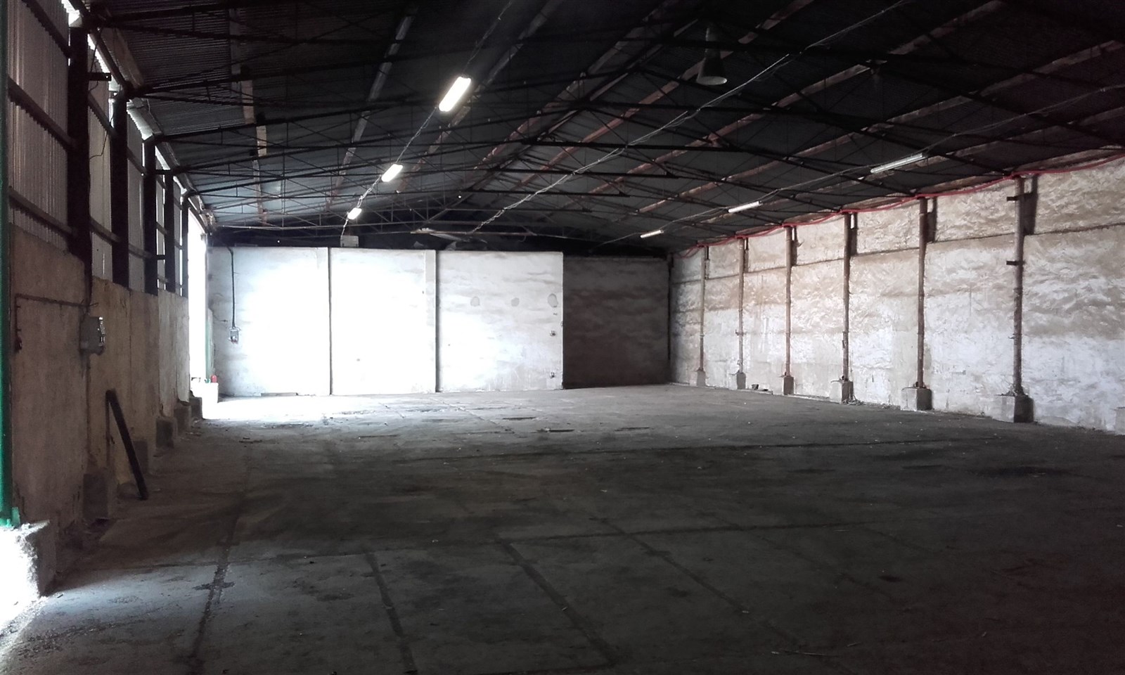 Průmyslový skladový prostor s betonovou podlahou a vysokým stropem, ideální pro skladování nebo výrobu, s dobrým osvětlením a velkými vjezdy.