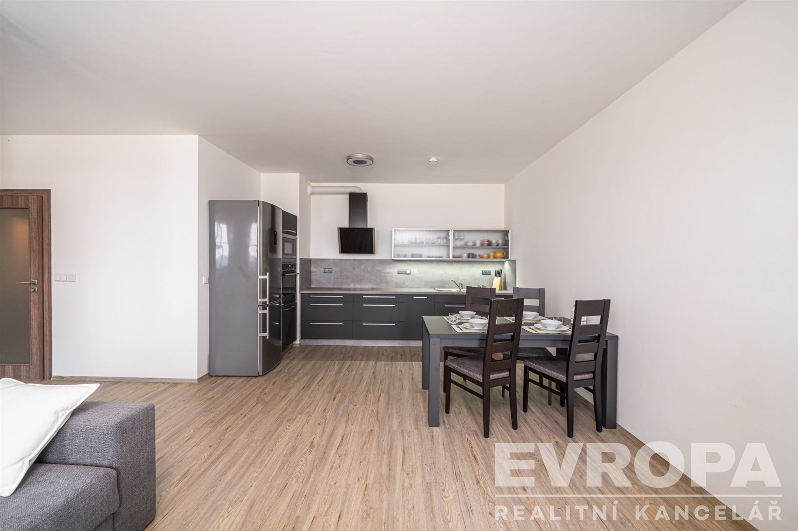 Moderní kuchyň s parketovou podlahou, vestavěné spotřebiče a jídelní kout. Interiér světlý s minimalistickým designem.
