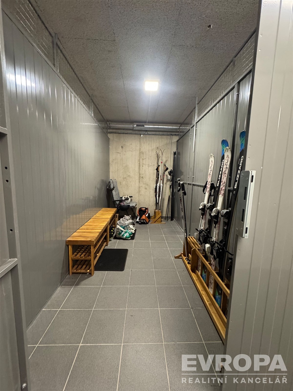 Úložný prostor s dlažbou, kovovými stěnami a úložnými lavicemi, ideální pro sportovní vybavení.