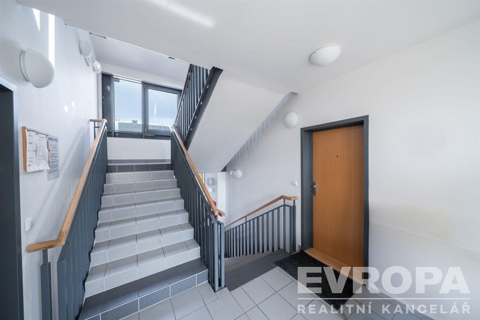 Moderní vstupní hala s dlažbou, světlým schodištěm a velkými okny. Vhodné pro rezidenční lokalitu s důrazem na čistý a udržovaný prostor.