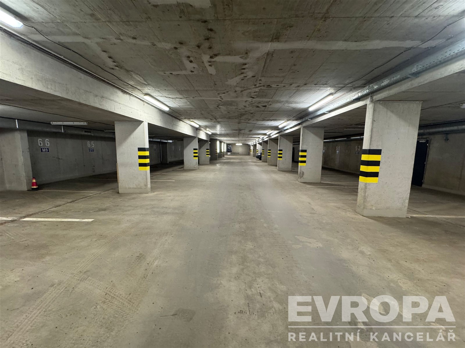 Podzemní garážové stání s betonovou podlahou, sloupy a dobrým osvětlením, ideální pro bezpečné parkování nebo skladování vozu.