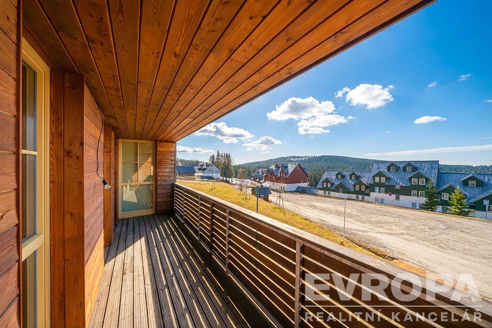 Prostorný balkon s dřevěnou podlahou a výhledem na okolní krajinu, moderní design a dřevěné obložení dodávají rustikální atmosféru.