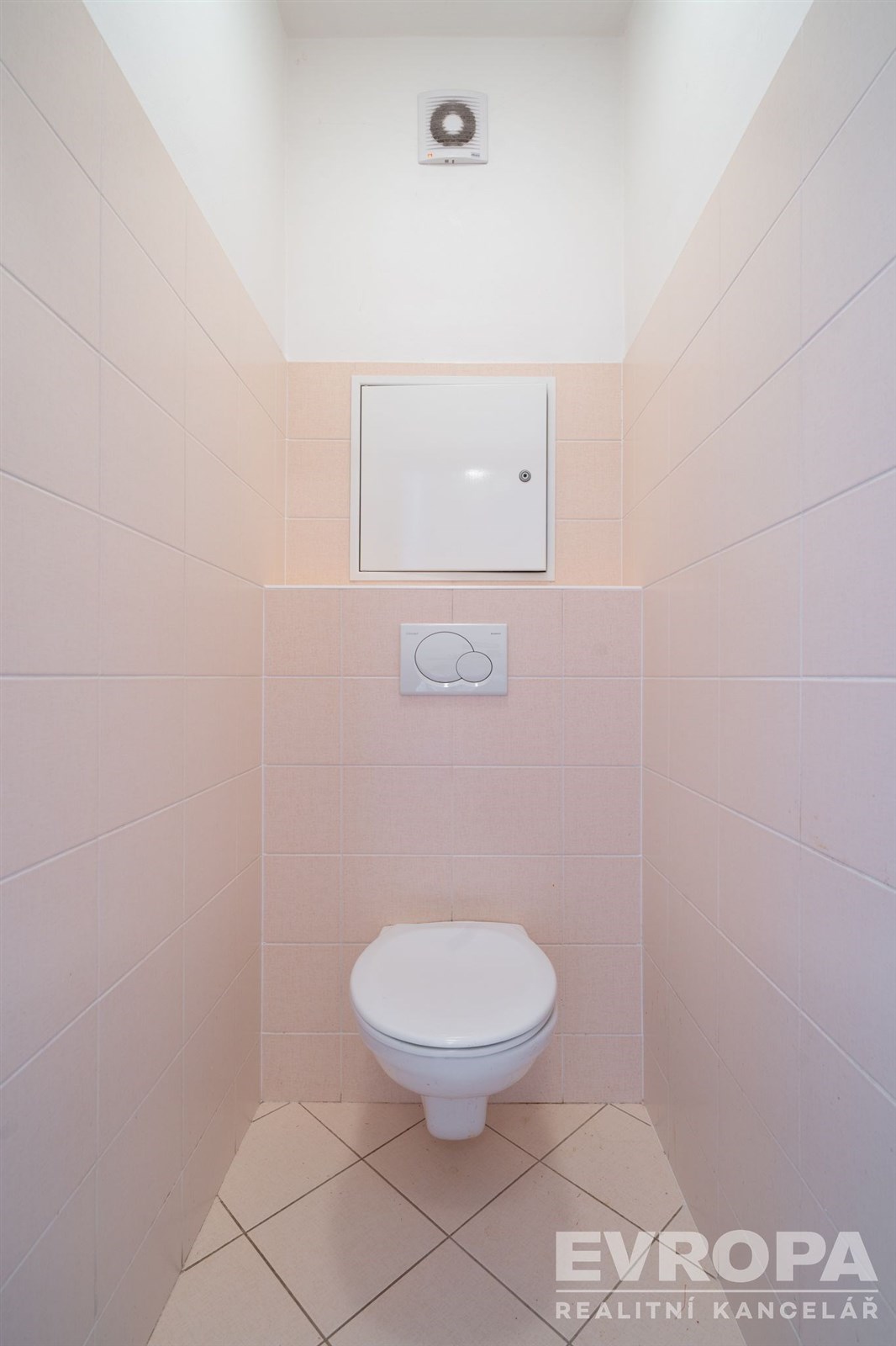 Moderní toaleta s béžovými kachličkami, nástěnným splachovacím systémem a dlažbou, minimalistický design, snadná údržba.