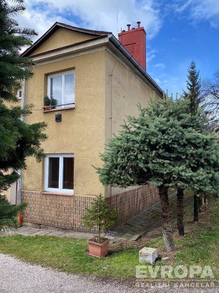 Dvoupodlažní rodinný dům s cihlovou fasádou, šikmou střechou a zahradou. Nachází se na klidném místě s vysokými jehličnany.