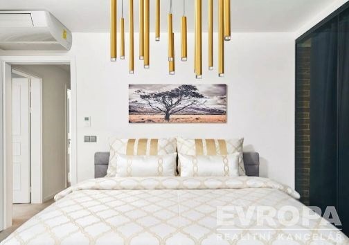 Prostorná ložnice, moderní styl s velkou postelí, zdobený lustr, světlé stěny a klimatizace, zajišťuje komfortní bydlení.
