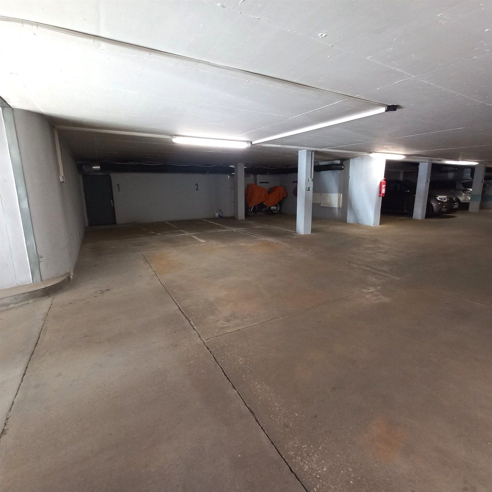 Podzemní parkoviště s betonovou podlahou nabízí prostorné parkovací místo a moderní osvětlení, ideální pro bezpečné uskladnění vozidel.