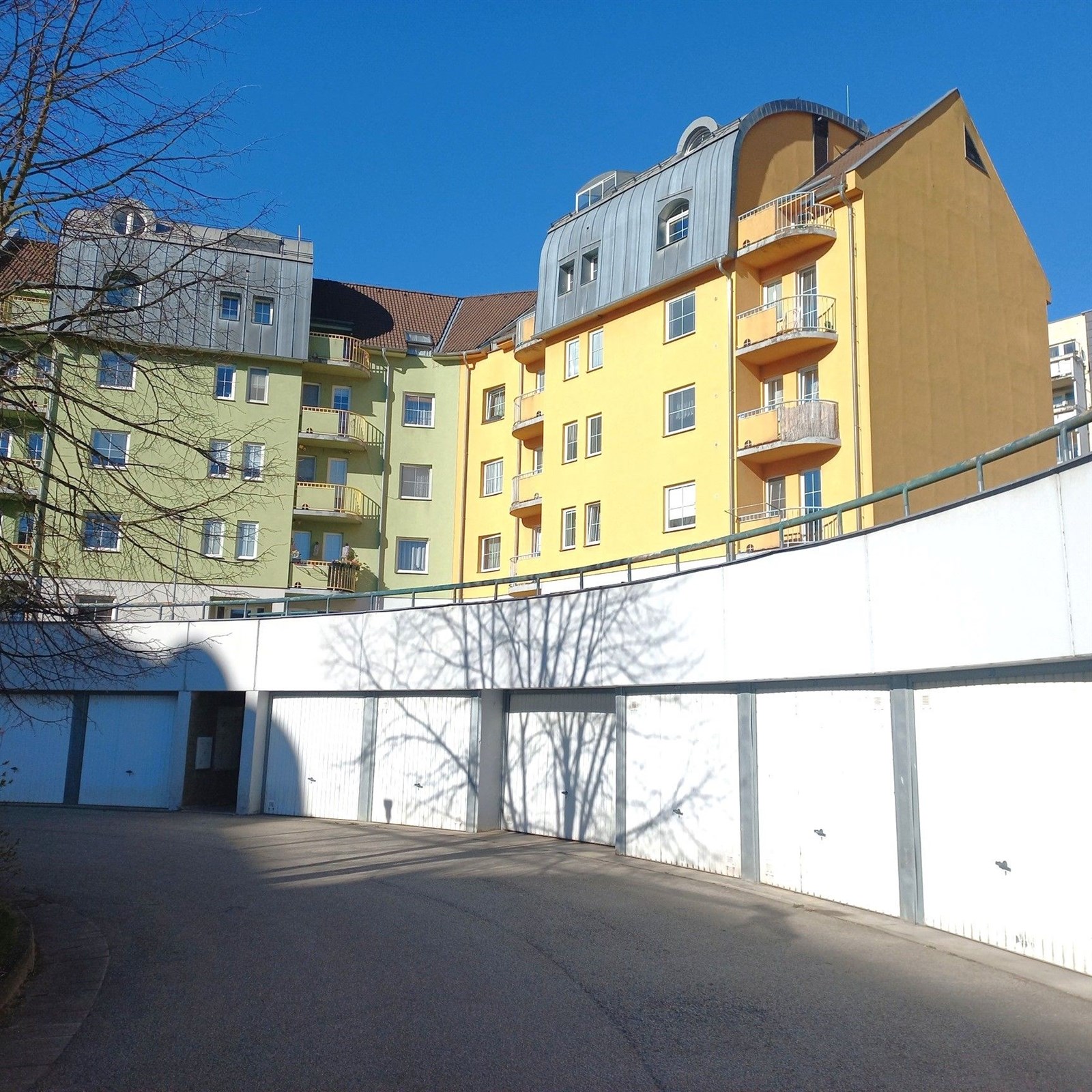 Vícepodlažní bytový dům s barevnou fasádou a balkonem, moderní architektura, umístění v klidné rezidenční čtvrti.