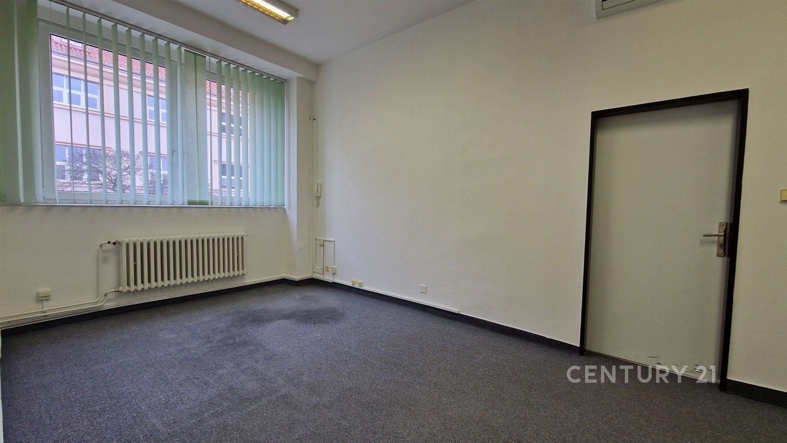 Prázdná kancelářská místnost s kobercovou podlahou, velkými okny a bílými stěnami, ideální pro komerční využití.