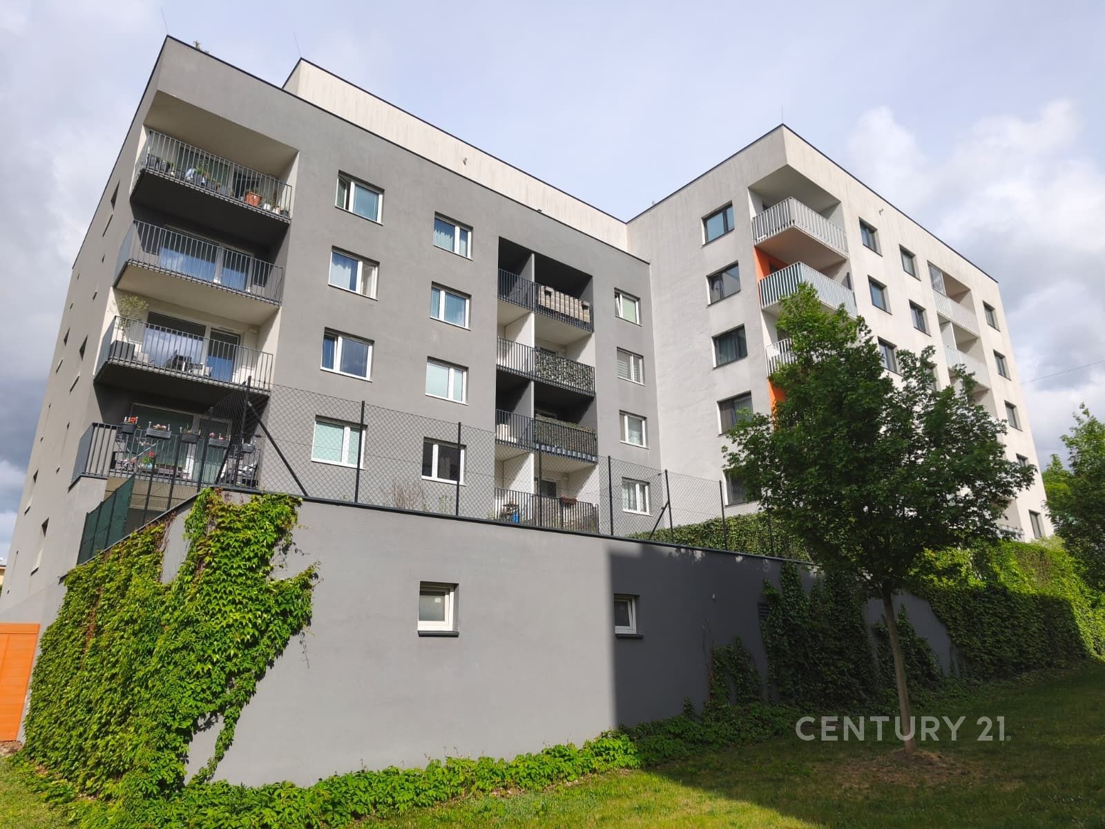 Moderní bytový dům s balkony, šedou fasádou a udrž