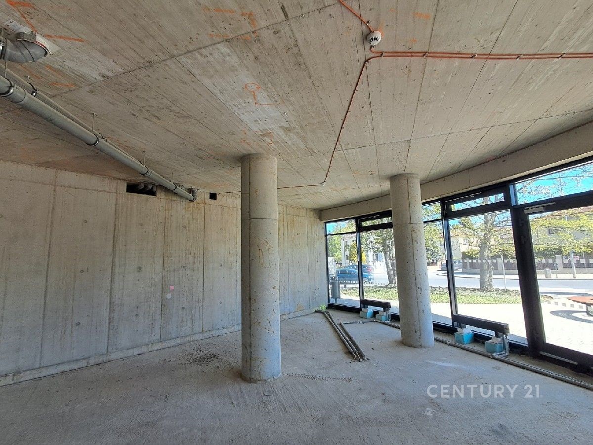 Světlý komerční prostor s betonovými stěnami, velkými okny a moderními konstrukčními prvky, ideální pro podnikání v atraktivní lokalitě.