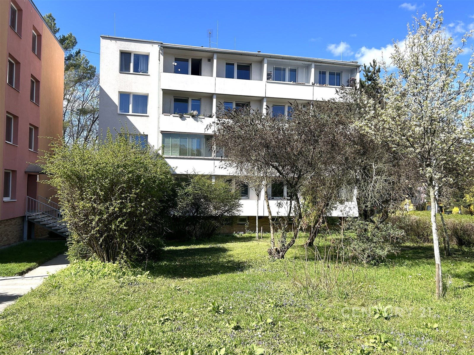 Čtyřpodlažní bytový dům s bílou fasádou, obklopený