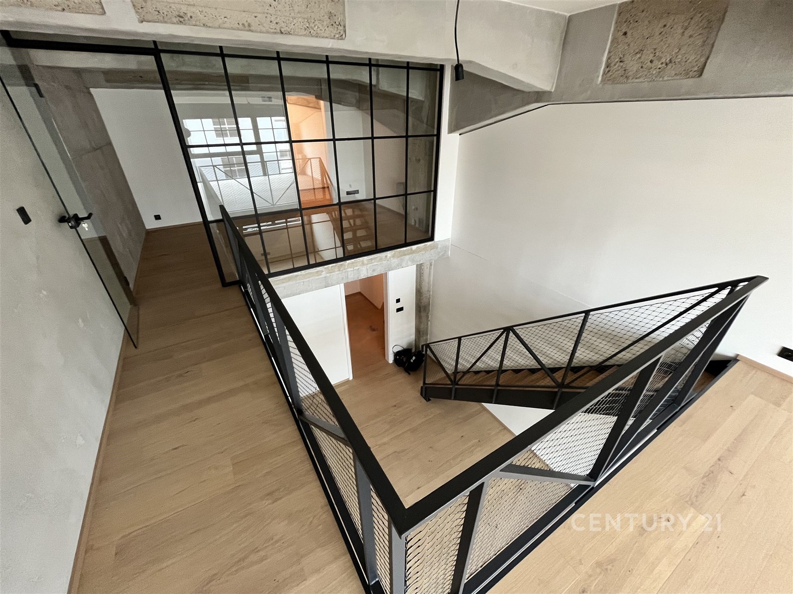 Chodba se skleněnou stěnou, parketovou podlahou a moderním zábradlím. Loftový styl s industriálními prvky, světlé prostory.