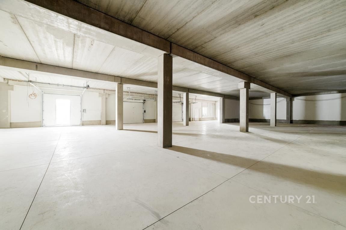 Prostorná garážová hala s betonovou podlahou, početné sloupy a vysoký strop. Nabízí ideální podmínky pro parkování nebo skladování.