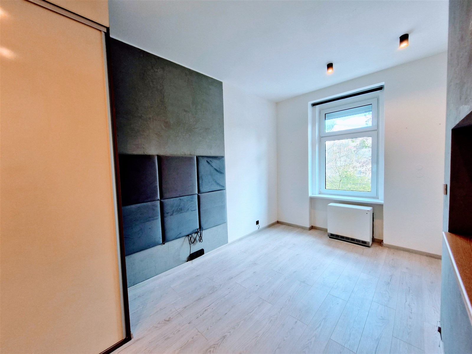 Světlá ložnice s parketovou podlahou a velkým okne