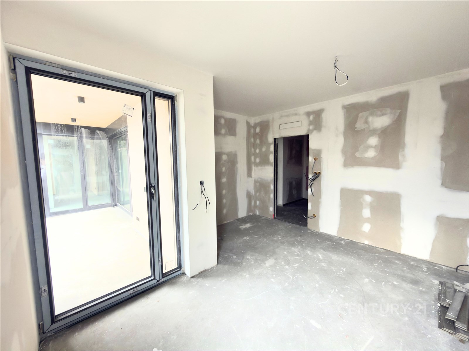 Prázdný pokoj s velkými okny, betonová podlaha, připraven k rekonstrukci, moderní dispozice, světlý interiér, vhodný pro úpravy.