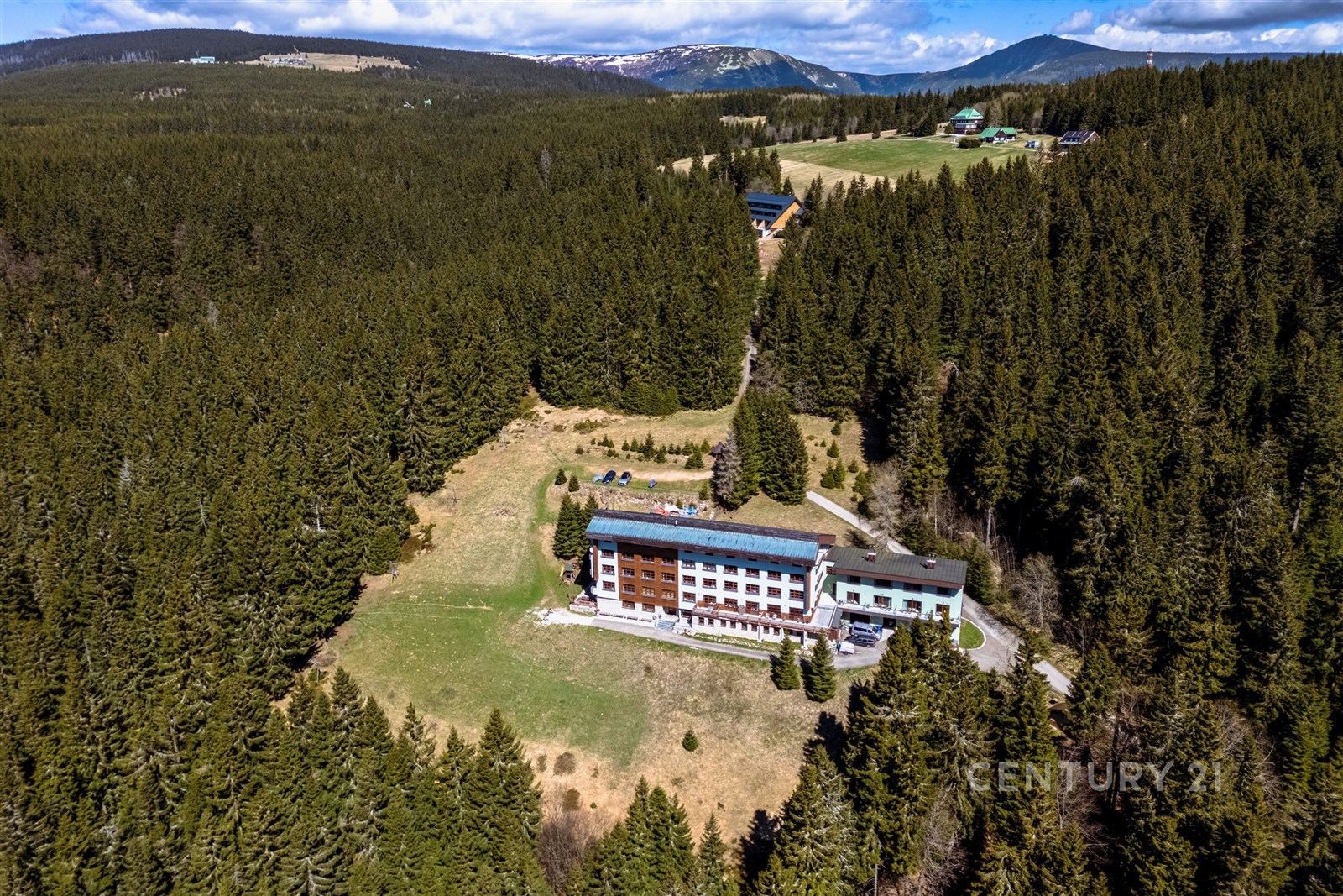 Poskytne výhled na hotel uprostřed lesa, obklopený zelenými stromy a horami na horizontu, ideální pro milovníky přírody.