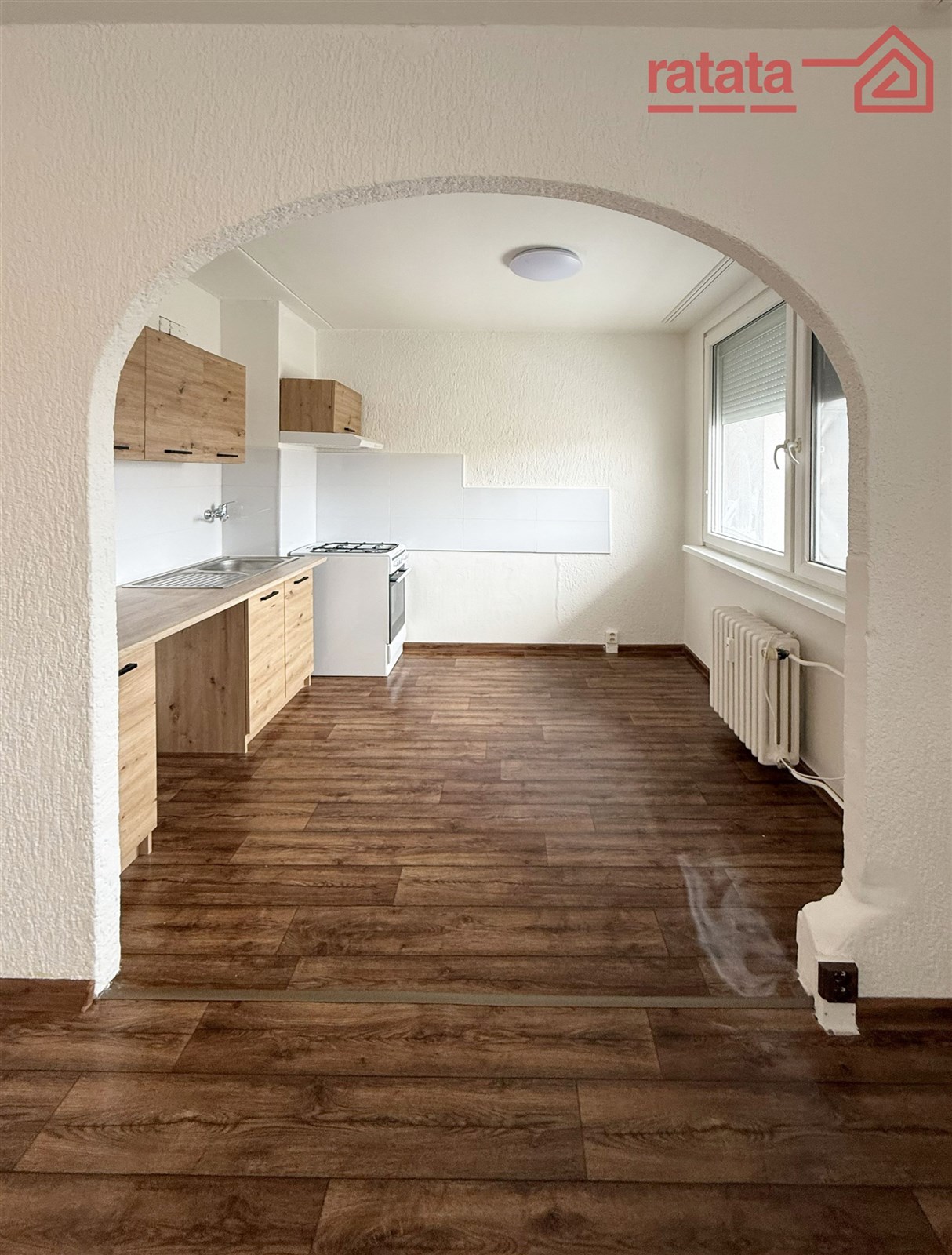 Moderní kuchyň s dřevěnou podlahou a vestavěnými skříněmi, světlé prostory s velkými okny pro maximální přirozené osvětlení.