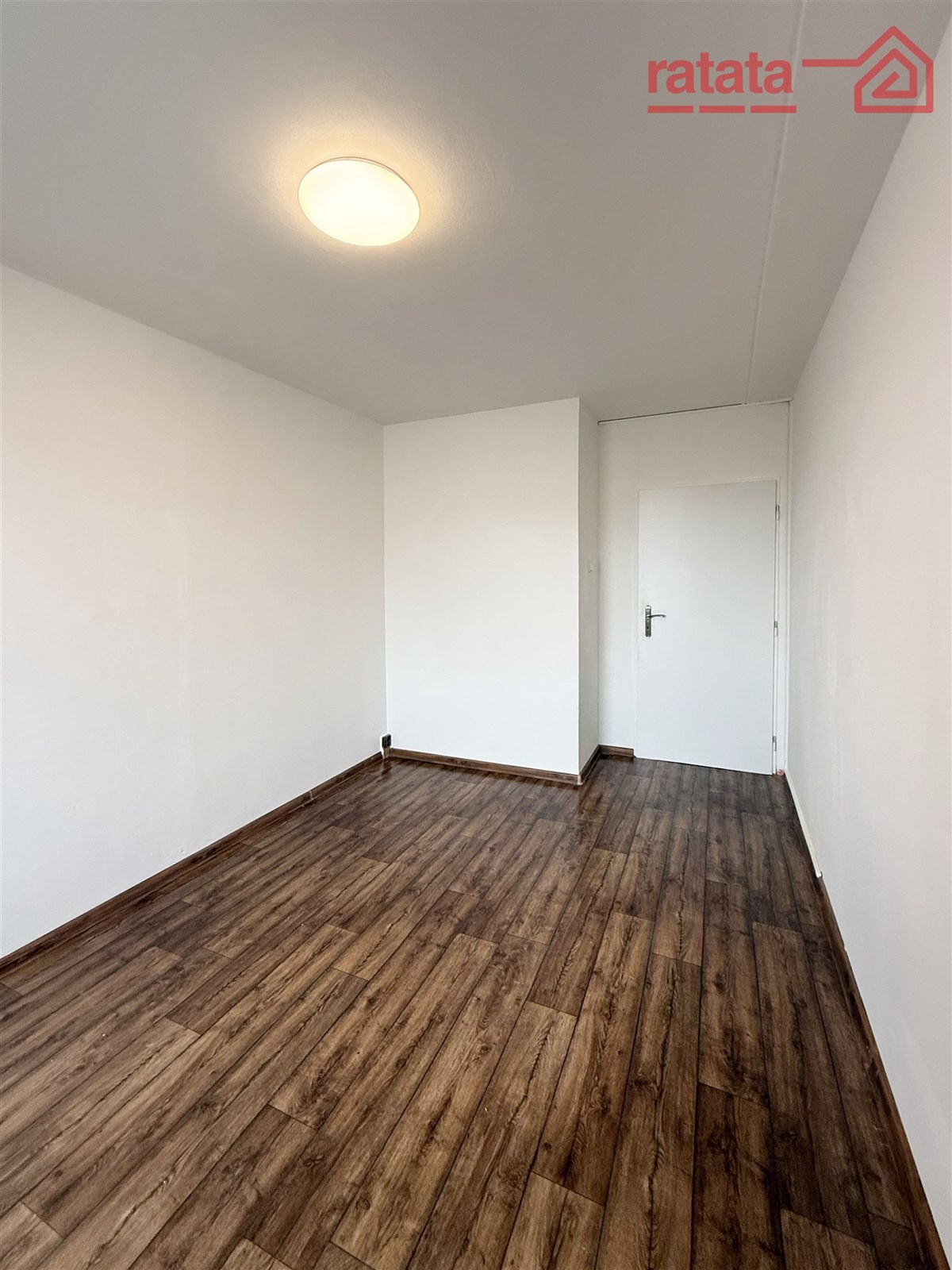 Prázdná místnost s parketovou podlahou, bílými stěnami a moderním osvětlením, ideální pro přizpůsobení vlastním potřebám.