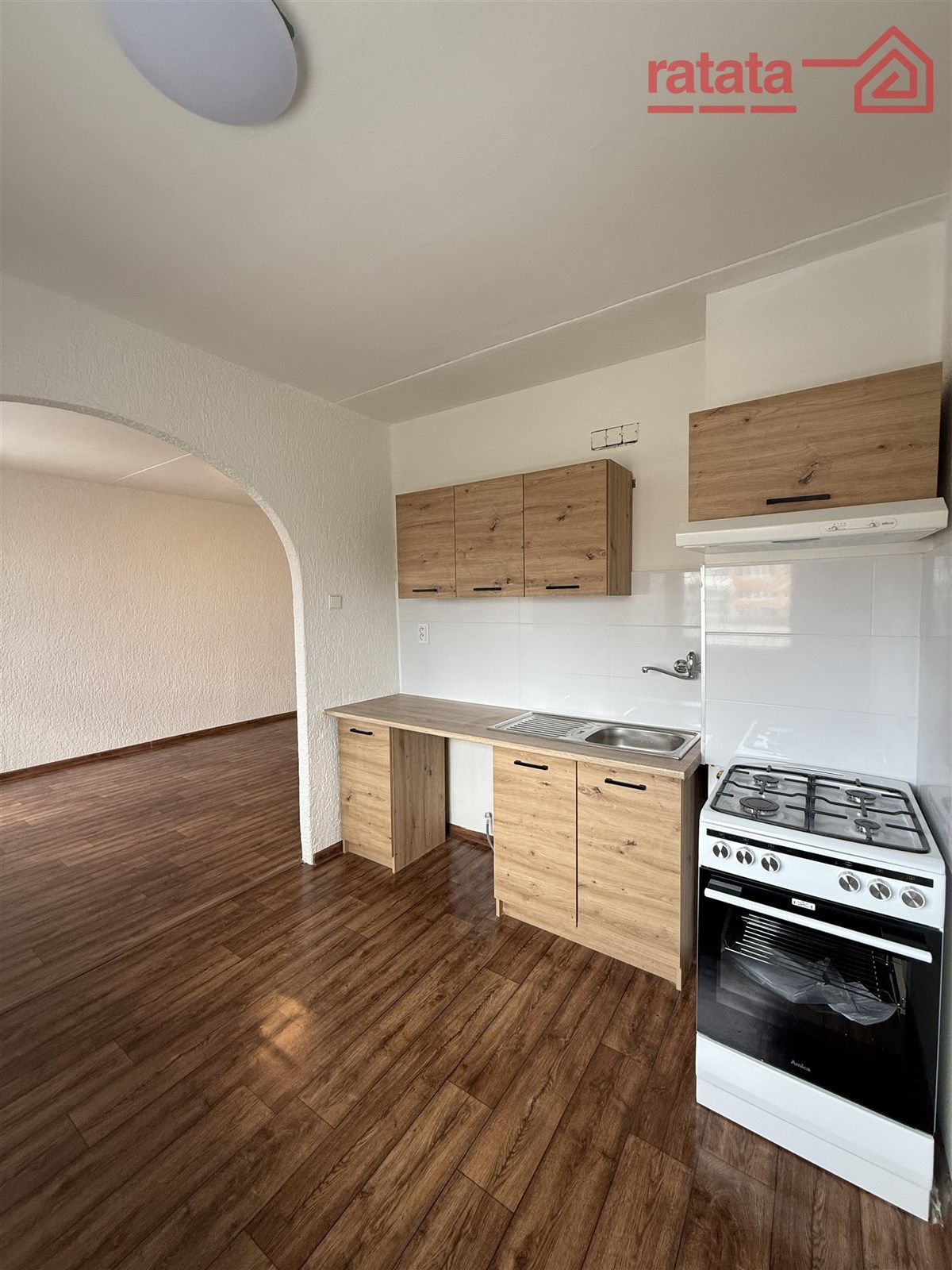 Kuchyň s laminátovou podlahou, světlé dřevěné skříňky, elektrický sporák, propojení s obývacím prostorem, moderní úpravy.