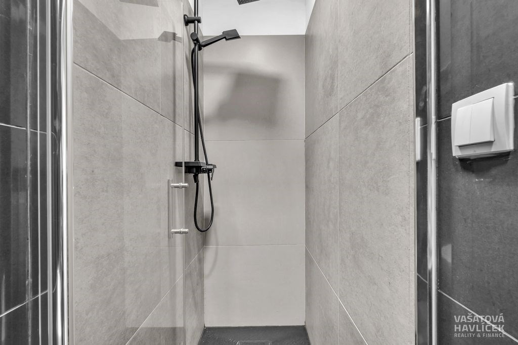 Moderní sprchový kout s hladkými šedými dlaždicemi, minimalistická černá sprchová hlavice a čisté linie poskytují elegantní vzhled.