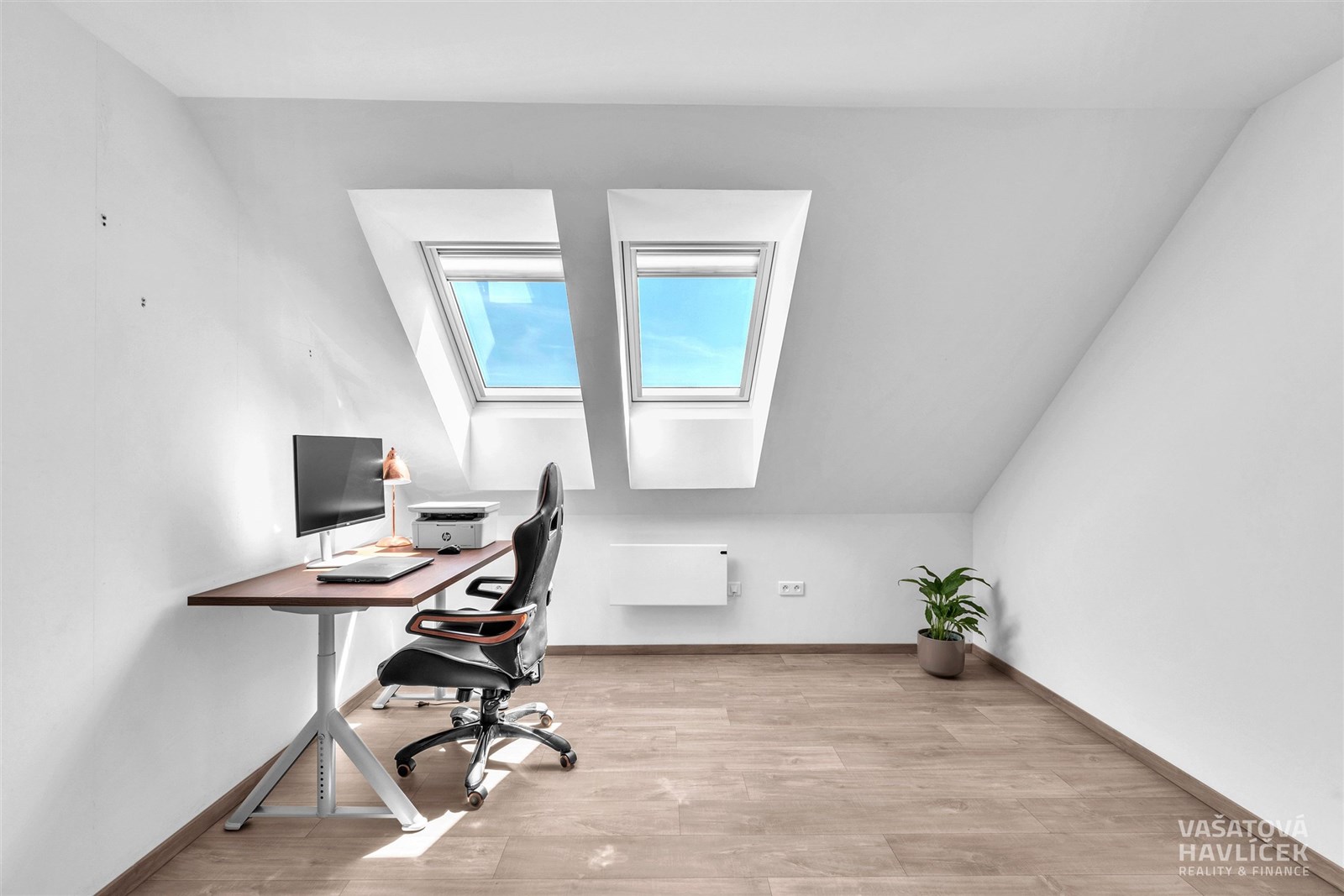 Podkrovní pracovna s moderními střešními okny, světlé dřevěné podlahy a minimalistickým designem vytvářejí funkční a stylový prostor.