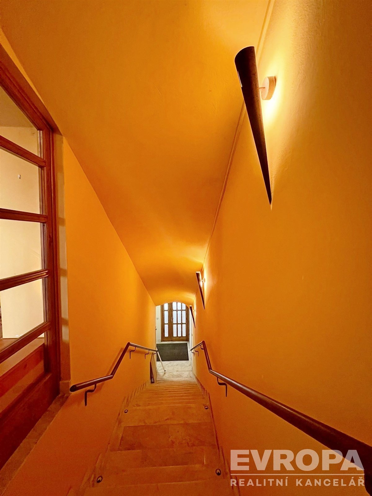 Chodba s osvětlením, dlažbou a schodištěm s dřevěným zábradlím, harmonicky spojuje prostory z přízemí.