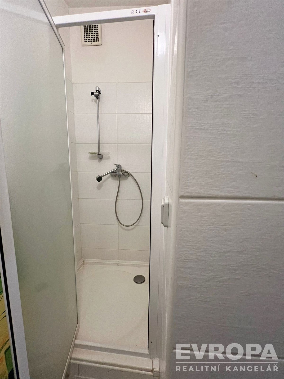 Koupelna se sprchovým koutem, bílá dlažba, světlá, moderní povrchy, úsporný design, čisté linie, stěny obložené kachličkami.