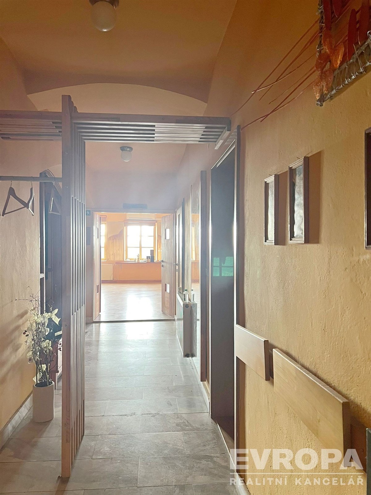 Chodba s dlažbou, vestavěnými skříněmi a velkými okny, která propouštějí světlo, působí útulně a moderně.