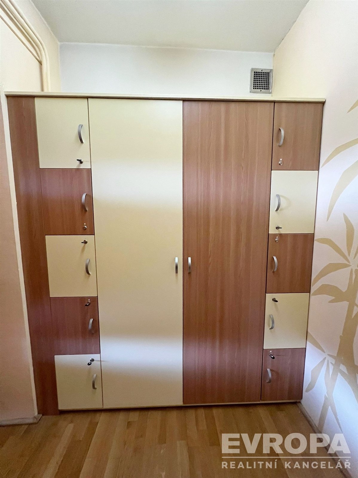 Vestavěná skříň s dřevěným dekorem, parketová podlaha v chodbě, praktické úložné prostory, moderní design.