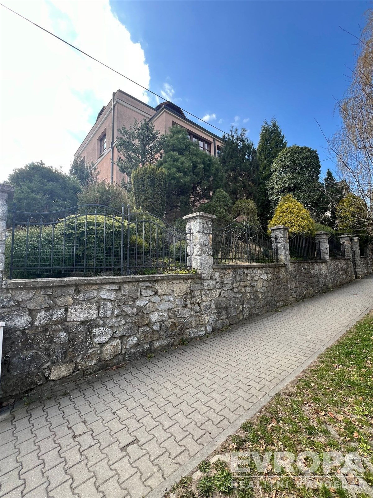 Vila s kamenným plotem, vzrostlá zeleň na zahradě 