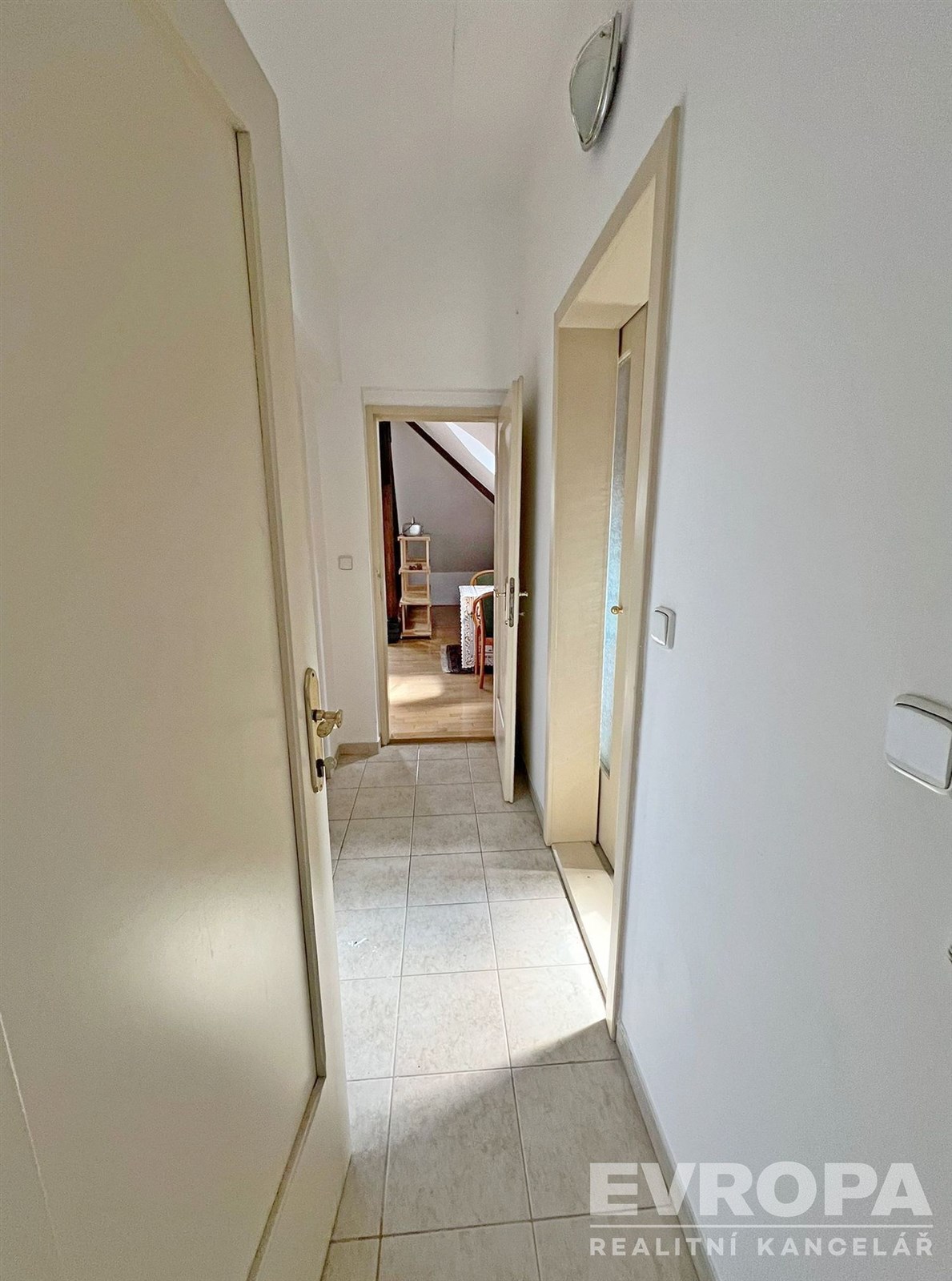 Úzká chodba s dlažbou, světlé stěny, moderní styl.
