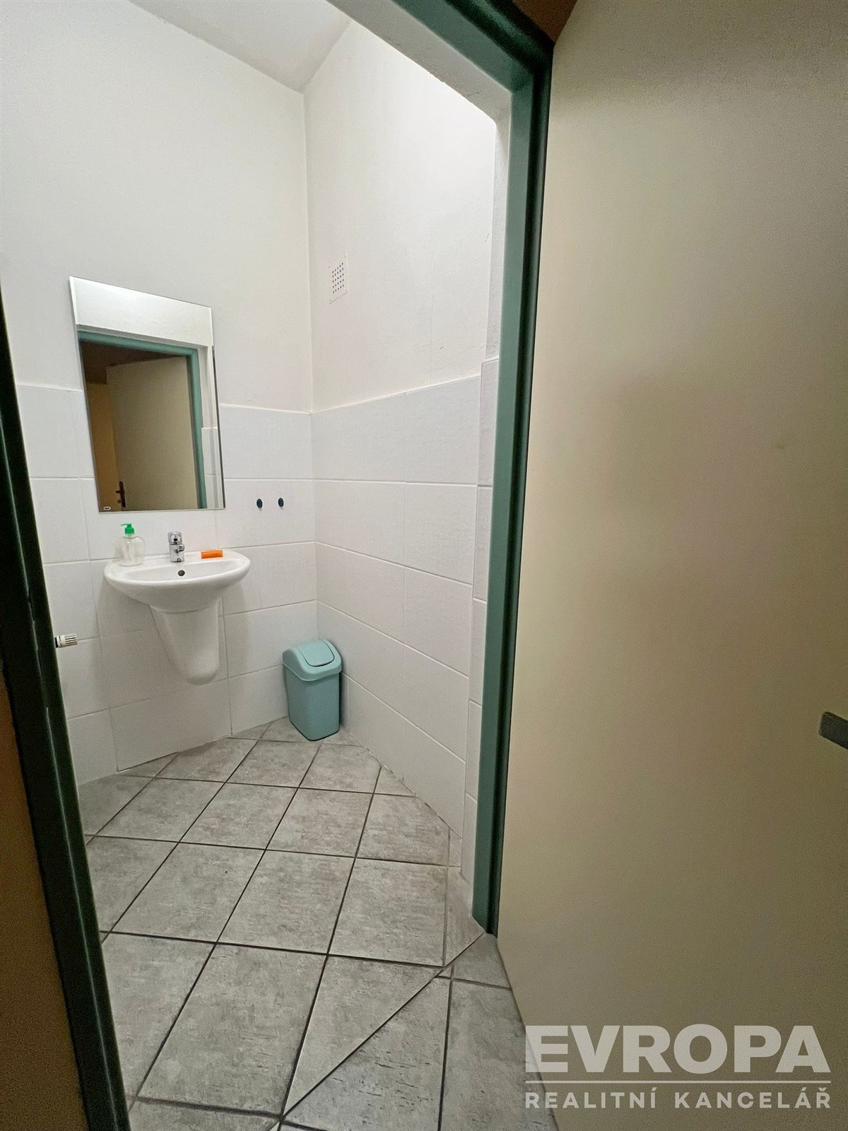 Malá koupelna s dlažbou, bílými obklady a závěsným umyvadlem, světlý interiér se zelenými doplňky, moderní jednoduchý design