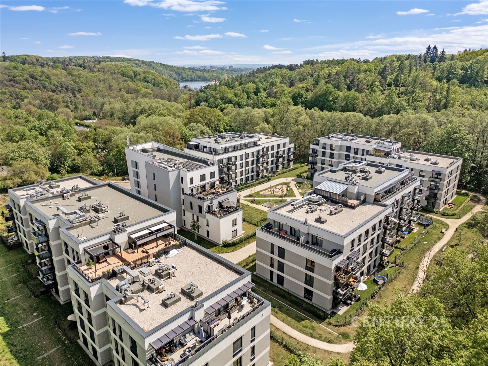 Moderní bytový komplex obklopený zelení, s prostornými balkony a bílou fasádou, nabízí klidné bydlení v blízkosti přírody.
