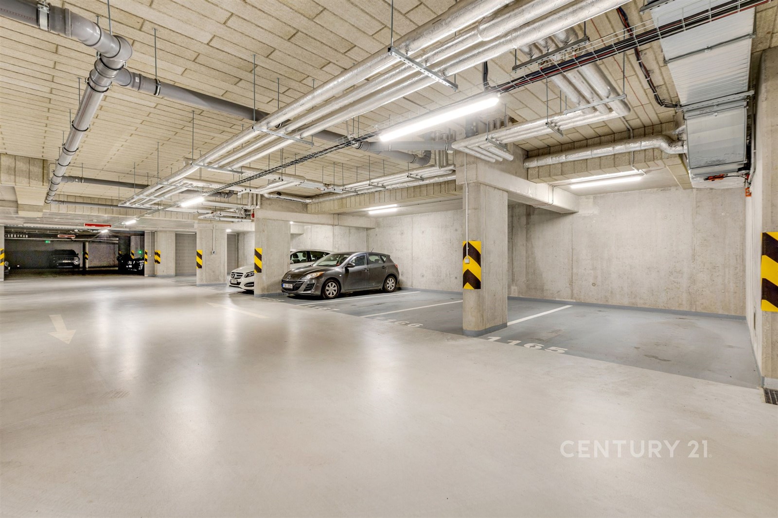 Podzemní parkovací garáž s moderními betonovými stěnami, dobrým osvětlením a vyhrazenými parkovacími místy, vhodná pro bezpečné parkování.