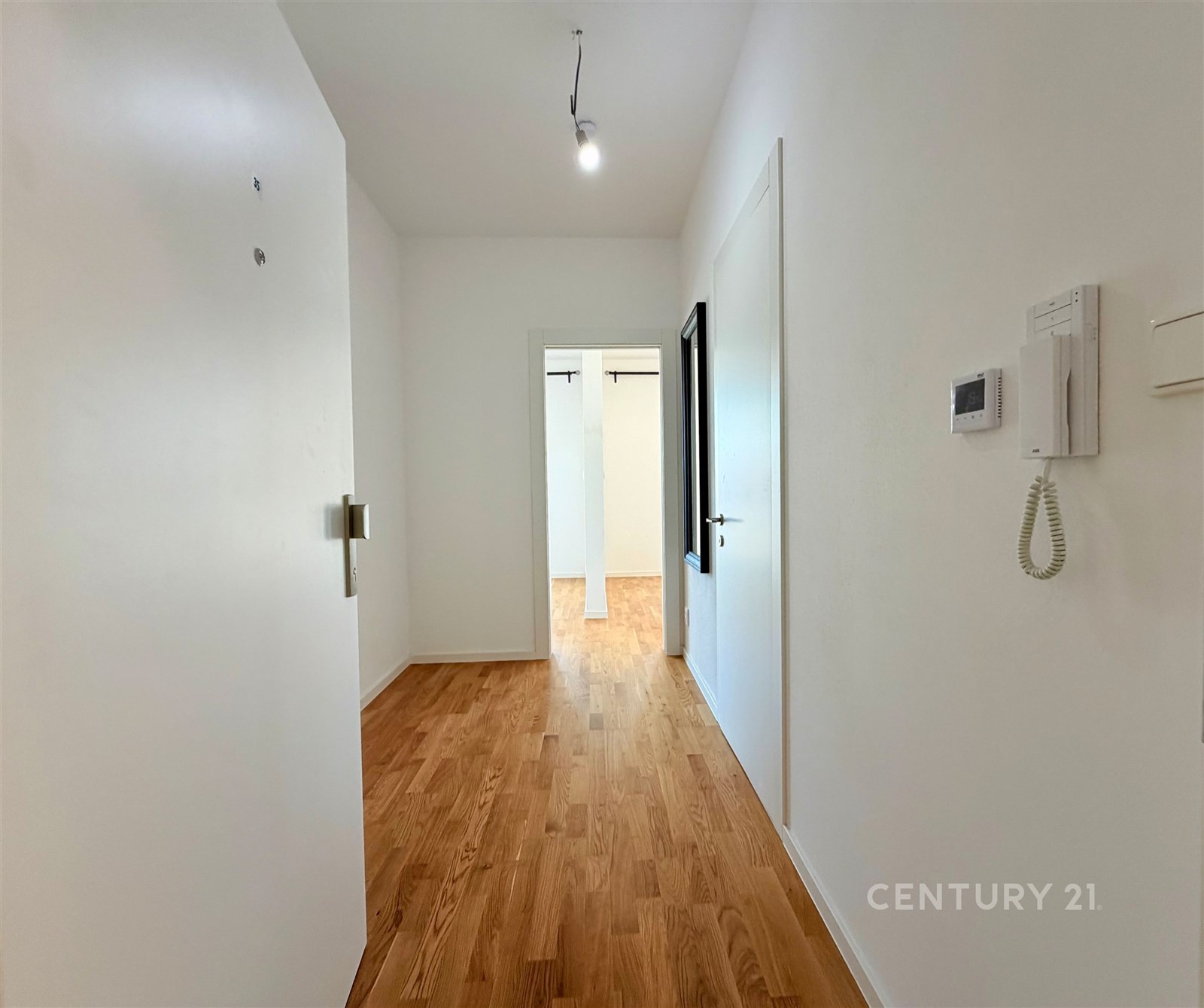 Světlá chodba s parketovou podlahou, moderní intercom a bílé stěny vytvářejí dojem prostorného a svěžího prostoru