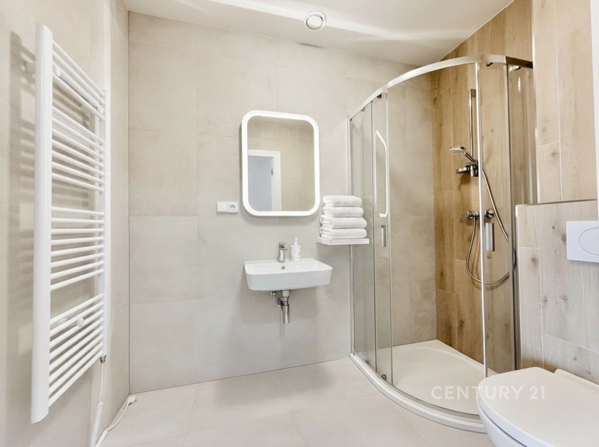 Moderní koupelna s velkoformátovou dlažbou, skleněným sprchovým koutem a designovým osvětlením, světlý a elegantní prostor